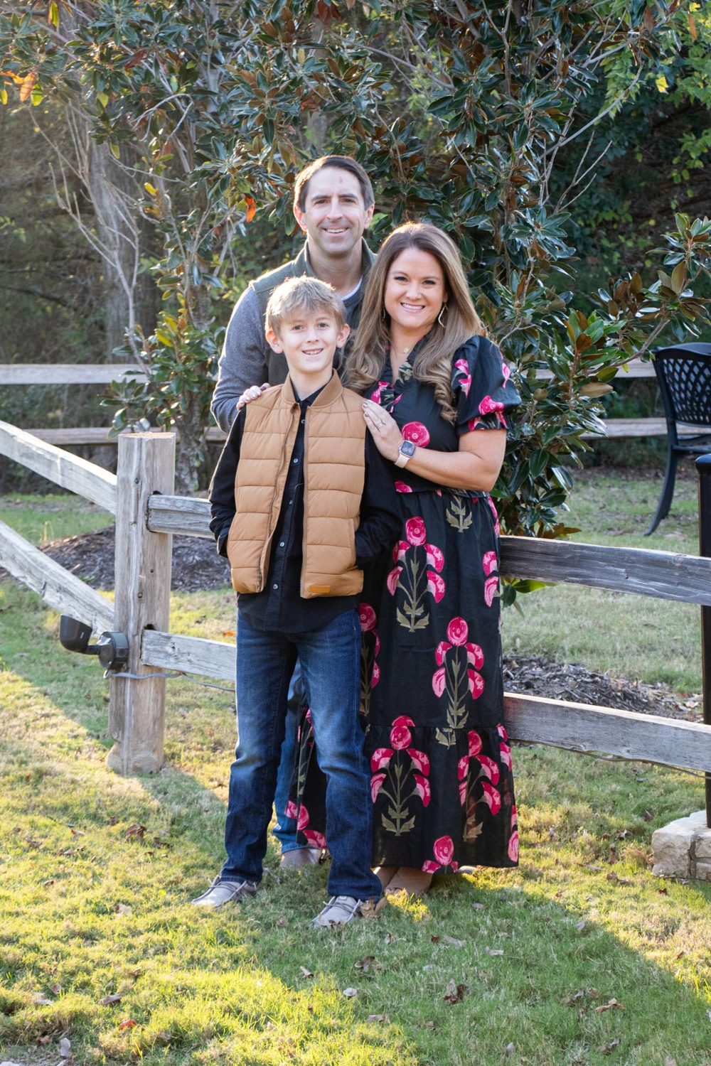 Family of three posing by a rustic fence in fall light